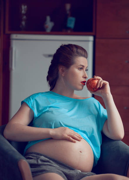 Studio shot of a pregnant woman holding a red apple and a heart shape stick synonymous of love and care. With copy space for text.