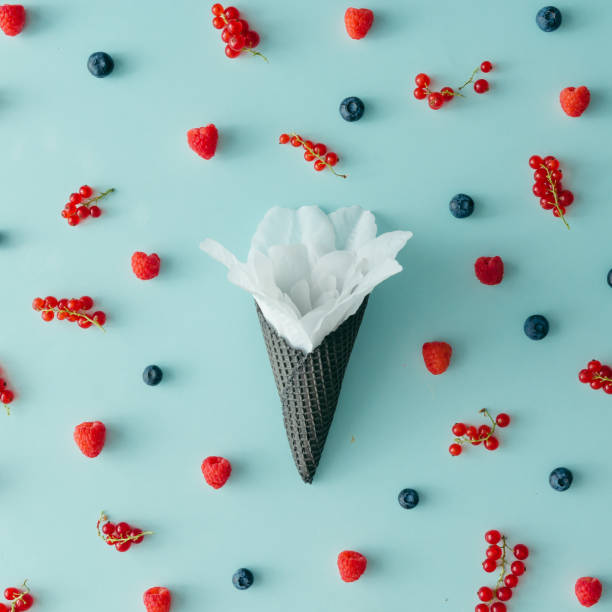 istock White flower in ice cream cone with forest fruit pattern. Flat lay. Summer concept. 810575840