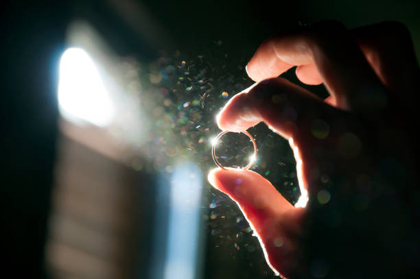 Hand holding the ring close up on background of ray of light in a dark dusty room. Valuing jewelry or getting married.