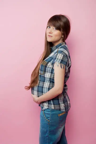 Pregnant woman in jeans and checkered shirt holding her belly. Happy mother-to-be.