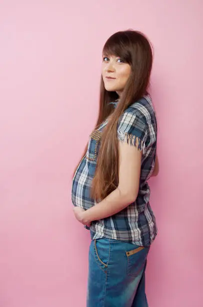 Pregnant woman in jeans and checkered shirt holding her belly. Happy mother-to-be.