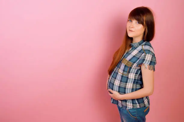 Pregnant woman in jeans and checkered shirt holding her belly. Happy mother-to-be.