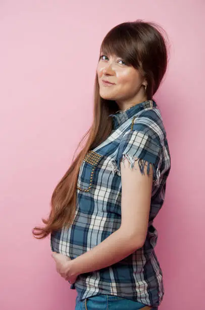 Pregnant woman in jeans and checkered shirt holding her belly. Happy mother-to-be.