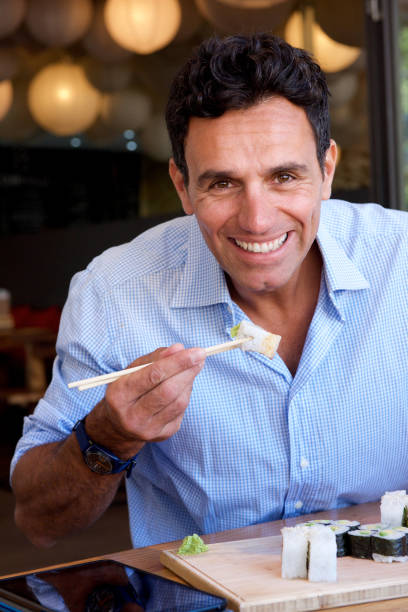 istock smiling businessman eating sushi with chopsticks 810599150