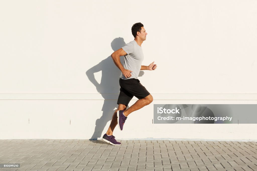 middle age man running by white wall Side portrait of middle age man running by white wall Running Stock Photo