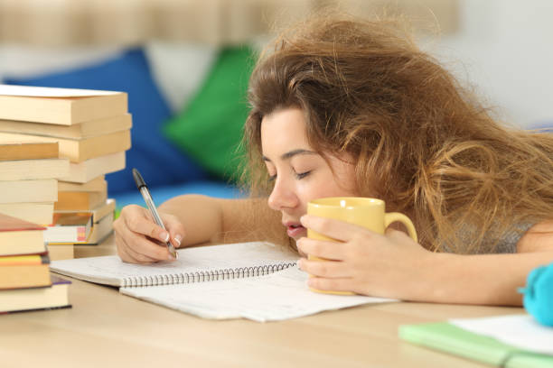 Tired and sleepy student trying to write notes Tired and sleepy student with tousled hair trying to write notes on a desk in her room in a house indoor narcolepsy stock pictures, royalty-free photos & images