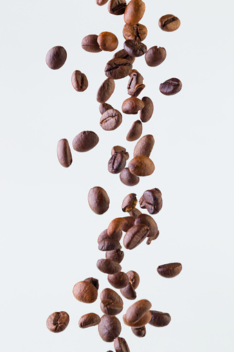 Grains of roasted coffee falling on white background, studio light