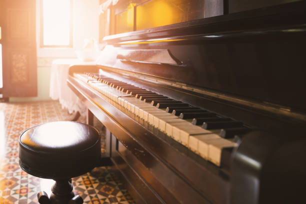 Side view of old and cracked piano and stool with orange warm tone from sunlight through window