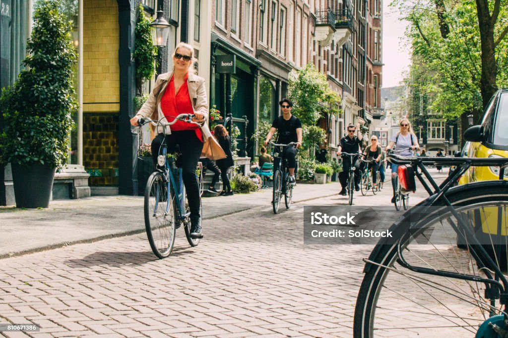Cyclist in Amsterdam Several people in Amsterdam cycling around the streets. Summer and trees and plants are seen outside the buildings. Cycling Stock Photo