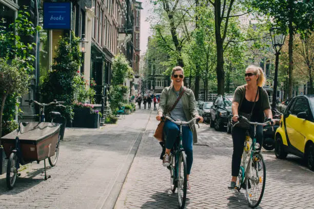 Women in Amsterdam cycling around the streets. Summer and trees and plants are seen outside the buildings.