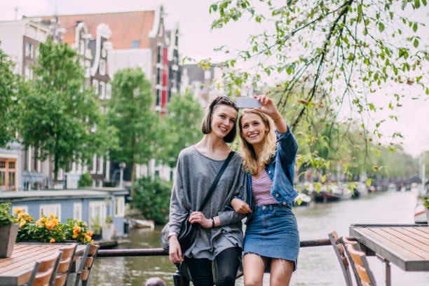 Selfie At Amstel River Female couple are taking a selfie together on a smart phone by Amstel River in Amsterdam. double denim stock pictures, royalty-free photos & images