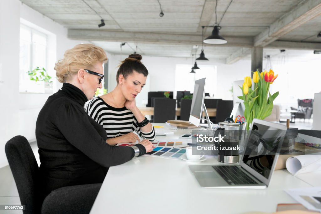 Senior businesswoman working together with young woman in the office Senior businesswoman working together with young woman in the office, looking at color samples. Color Swatch Stock Photo