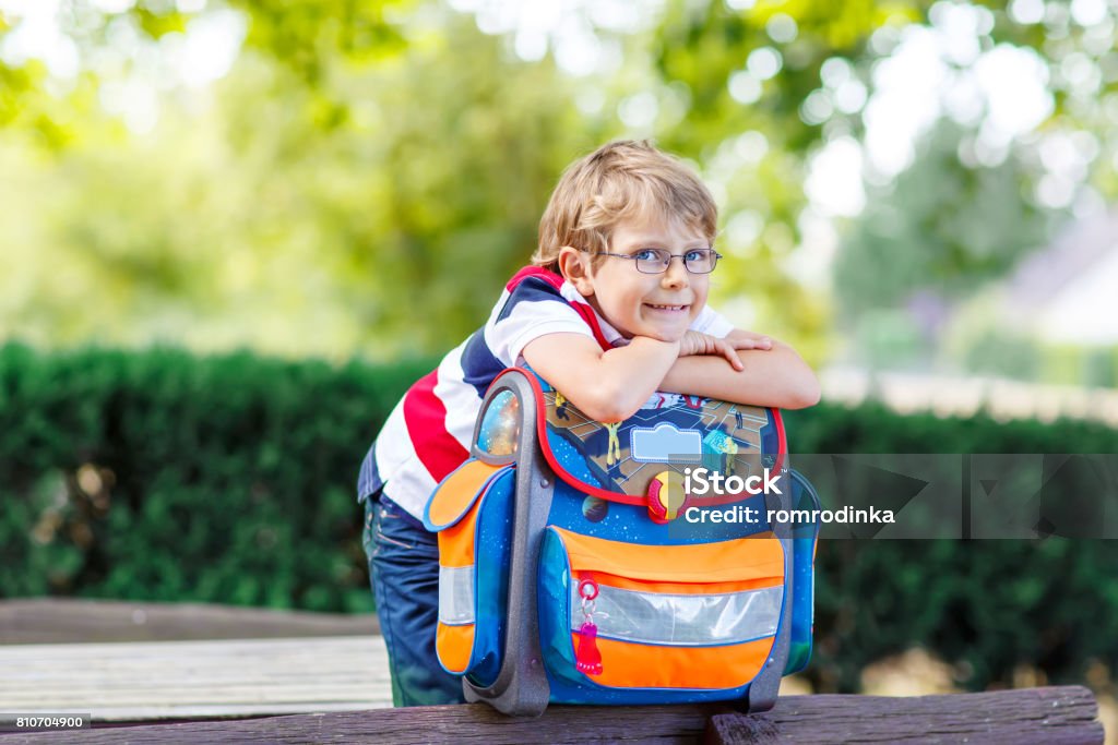 little kid boy with school satchel on first day to school Happy little kid boy with glasses and backpack or satchel on his first day to school . Child outdoors on warm sunny day, Back to school concept. Kid with traditional schoolbag in German Schultuete First Day Of School Stock Photo