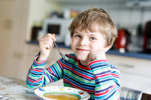istock Adorable little school boy eating vegetable soup indoor. 810711208