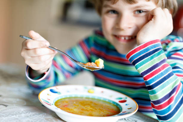 istock Adorable little school boy eating vegetable soup indoor. 810712824