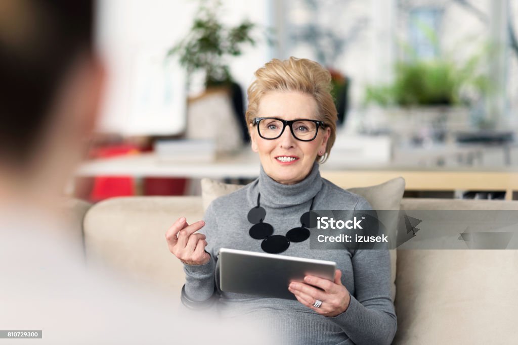 Senior adviser talking with young woman Senior woman talking with young businesswoman, giving advices, holding a digital tablet in hand. Digital Tablet Stock Photo