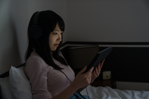 Young woman relaxing and looking at a digital tablet on her bed