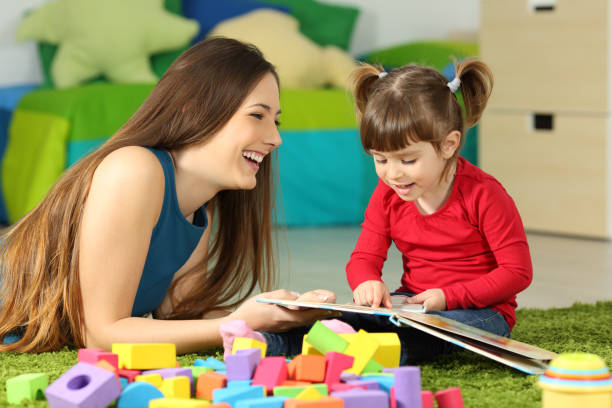 Mother and toddler playing with a book Mother and toddler playing together with a book lying on the floor in the bedroom at home with a colorful background nanny stock pictures, royalty-free photos & images