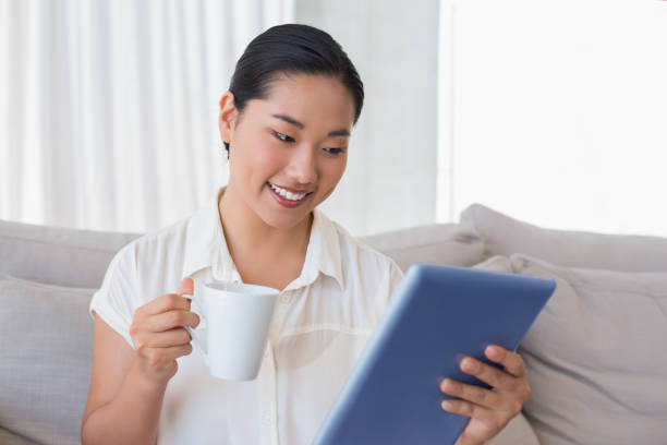 istock Smiling woman sitting on couch using tablet pc having coffee 810774038
