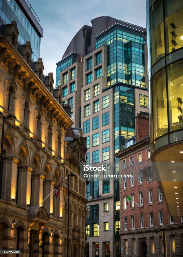 Traditional and modern city-centre architecture in Manchester at dusk Illuminated office buildings in the English city of Manchester, with a mixture of old and new architecture. Manchester - England Stock Photo