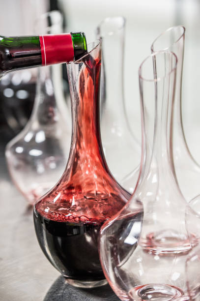 сомелье на работе, наливая вино декантеру, стоя возле винной полки - wine decanter elegance pouring стоковые фото и изображения