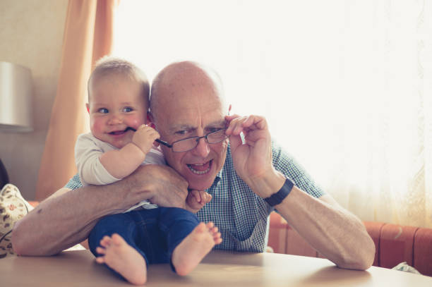 Grandfather playing with baby at table A grandfather is playing with a little baby who is grabbing his glasses old man baby stock pictures, royalty-free photos & images