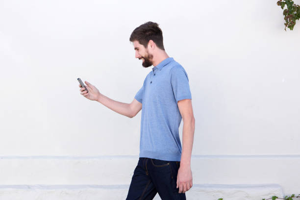 istock smiling man walking and looking at mobile phone 810797648