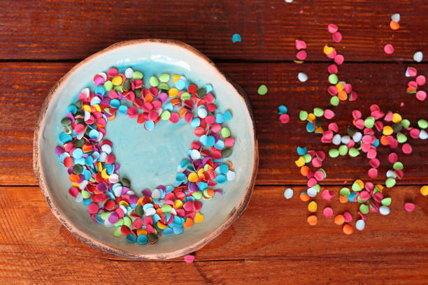 istock Heart from multicolored confetti on small turquoise handmade ceramic plate on background of wooden boards. Bright true love and romance 810808514