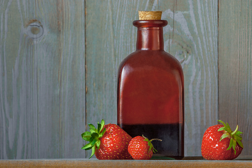 Freshly picked strawberries and a red glass bottle with strawberry syrup stand on a table in a rural house