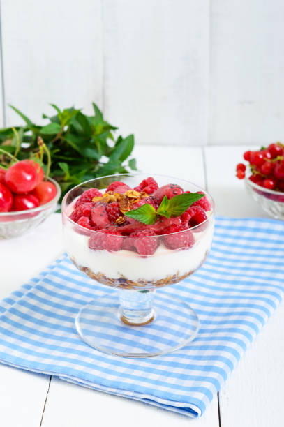 doce sobremesa cremosa com cereais, queijo creme, framboesas frescas em uma tigela de vidro em um fundo branco de madeira. - raspberry ice cream close up fruit mint - fotografias e filmes do acervo