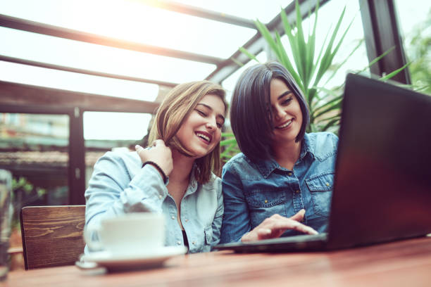 istock Two Female Frineds Using Laptop and Laughing in Coffee Shop 810868774