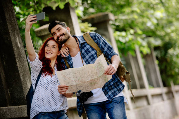 istock Young tourist couple with map taking selfie 810874436