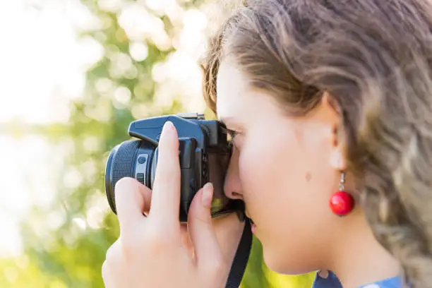 Closeup side profile view of young woman taking a picture looking through camera outdoors in green park and river