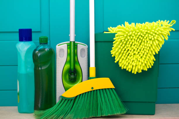 Green broom, garbage pail and green cleaning supplies in front of a vibrant green background.