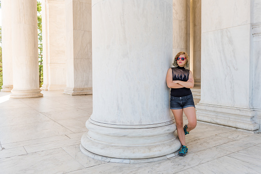 Young woman leaning on marble column in Jefferson Memorial in Washington, DC wearing red sunglasses