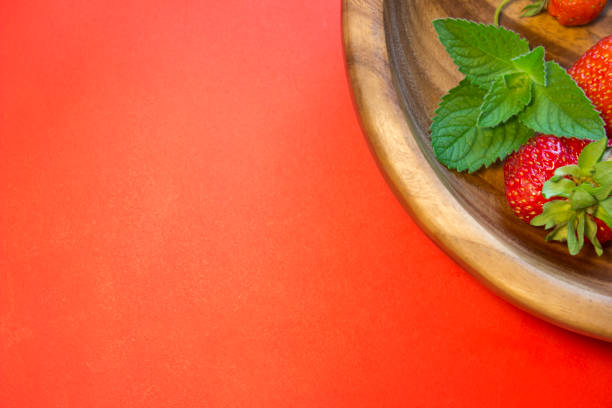 Tasty strawberries and a mint leaf in a wooden plate on a red background. Top view composition. Place for text.