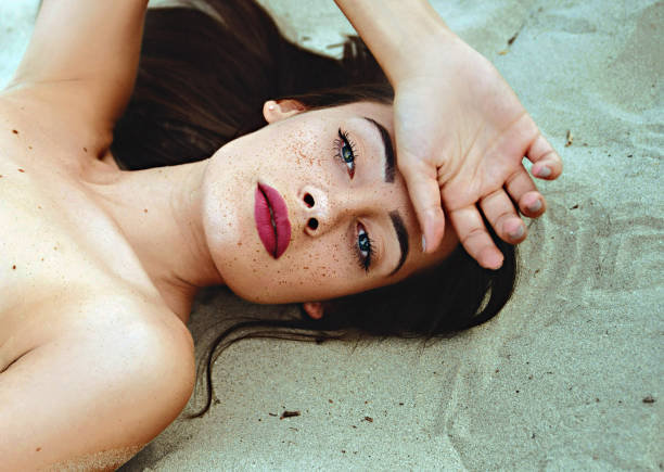 Portrait of beautiful brunette with freckles laying on sand