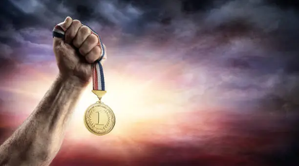 athlete Hand Holding Gold Medal With Sunset Background