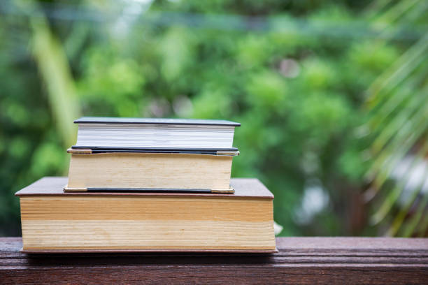 istock Old book stack on wood table over blurred natural green garden background 811081616