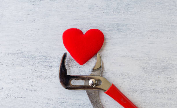 istock Pliers holding red heart on white wood background 811083942
