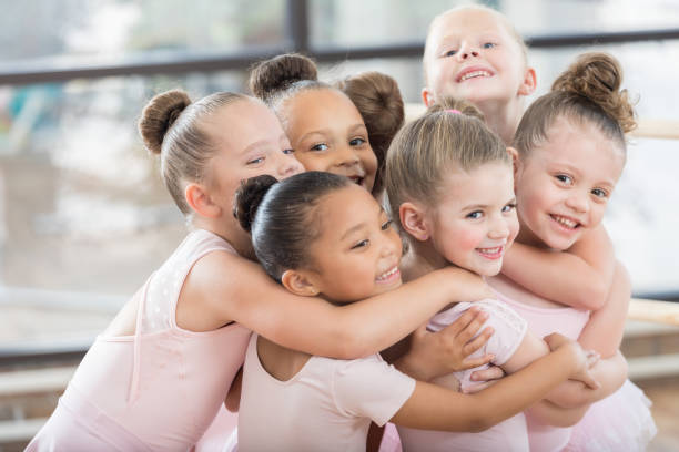 Young ballerinas form a smiling group hug A group of young smiling ballerinas hug each other in a large huddle.  Three of them are looking at the camera. ballerina stock pictures, royalty-free photos & images