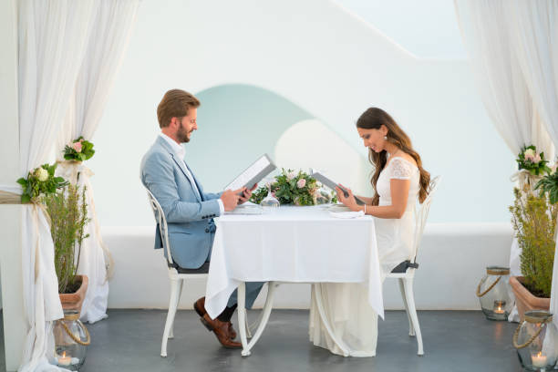 couple reading the menu in a romantic setting vacation honeymoon private table for two in wedding decoration outside on terrace of luxury restaurant in greece, newlywed couple sitting and choosing from menu exclusive dinner stock pictures, royalty-free photos & images
