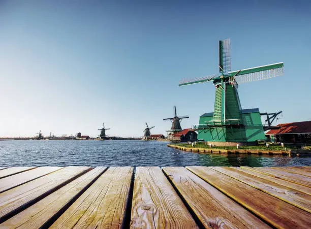 Photo of Colorful spring day with traditional Dutch windmills canal in Rotterdam. Wooden pier near the lake shore.