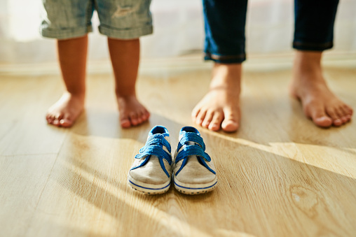 Shot of an unidentifiable mother and her little boy's feet standing behind a pair of baby shoes at home