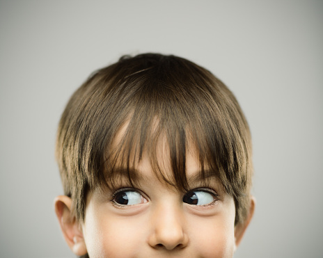 Close up portrait of happy little boy looking away with surprise against gray background. Horizontal shot of real kid smiling in studio. Photography from a DSLR camera. Sharp focus on eyes.
