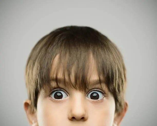 Close up portrait of surprised little boy with raised eyebrows. Horizontal shot of real kid on gray background. Photography from a DSLR camera. Sharp focus on eyes.