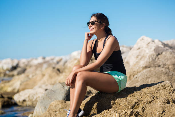 istock Young happy woman sitting on seaside rock smiling 811259018