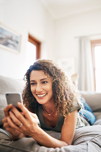 Shot of a happy young woman using her smartphone while relaxing on the couch at home