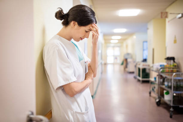 Upset female nurse standing in hospital corridor Upset female nurse standing in hospital corridor. Medical professional looking unhappy. female nurse stock pictures, royalty-free photos & images