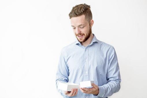 Closeup portrait of smiling young man holding two different size boxes. Isolated front view on white background.